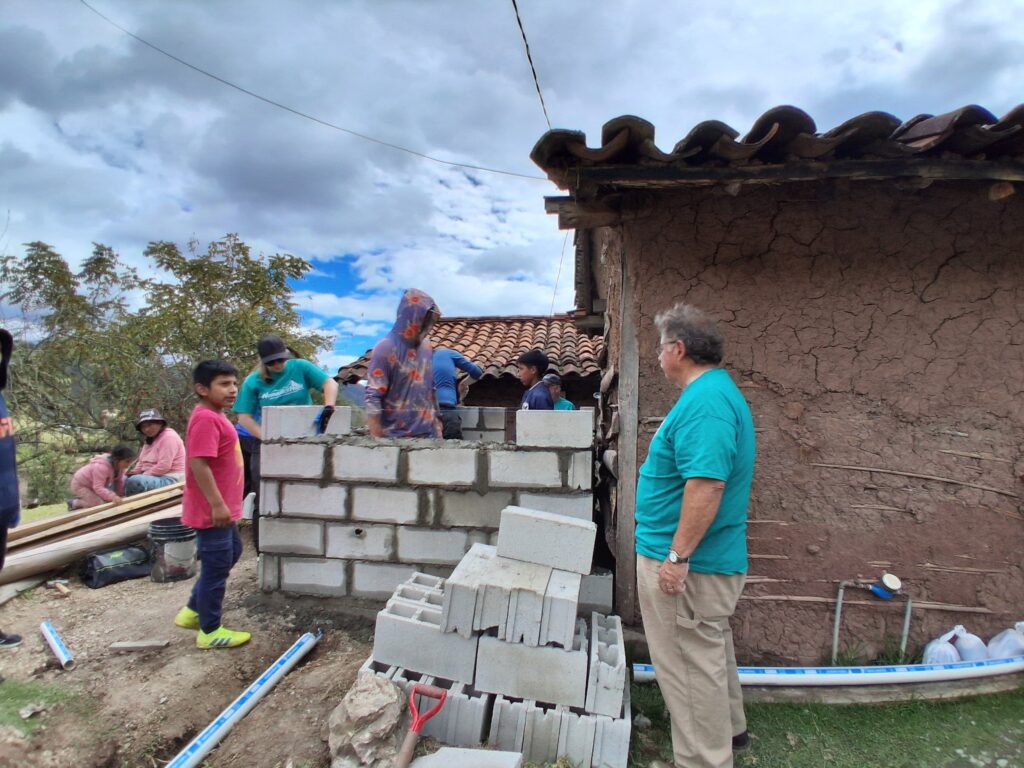 Volunteers and neighbors build the block walls of a new bathroom beside an adobe house in Jadán