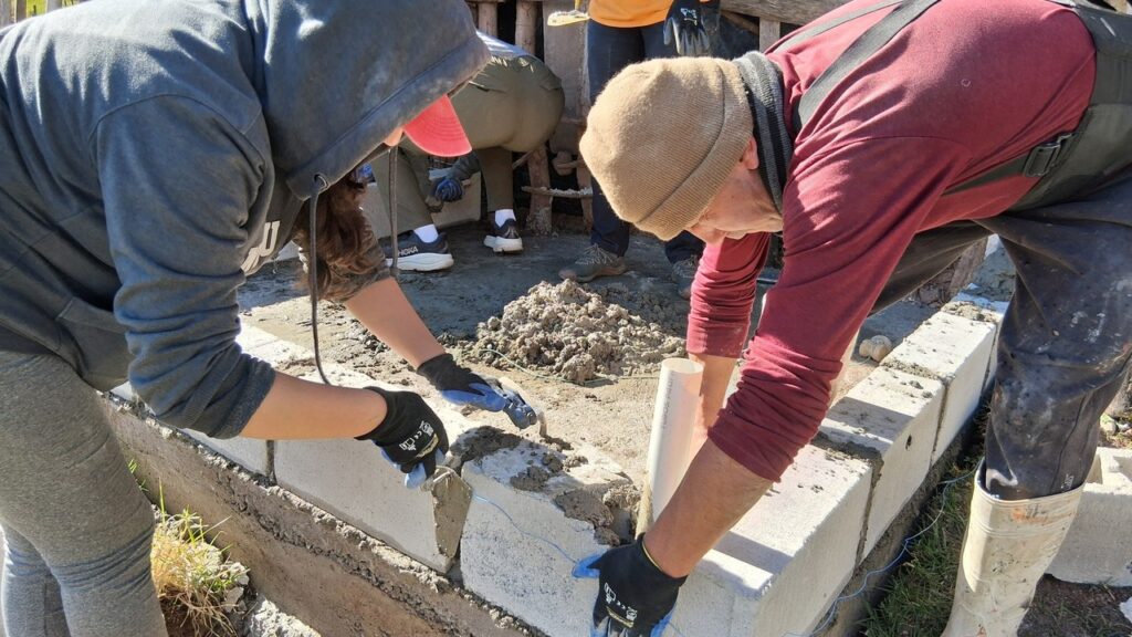 Two volunteers laying concrete blocks and mortar for a bathroom wall in Jadán